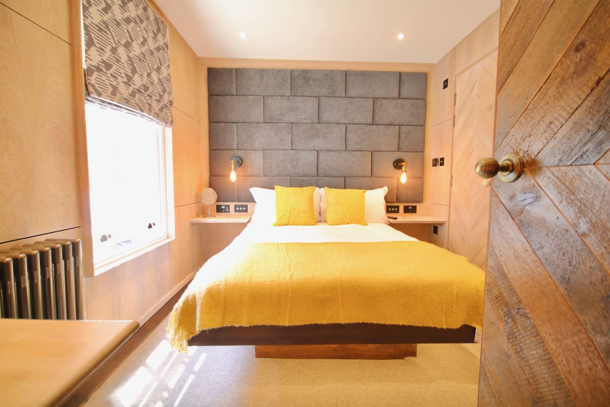 A modern bedroom with a large bed, wooden paneling, and a window with blinds.