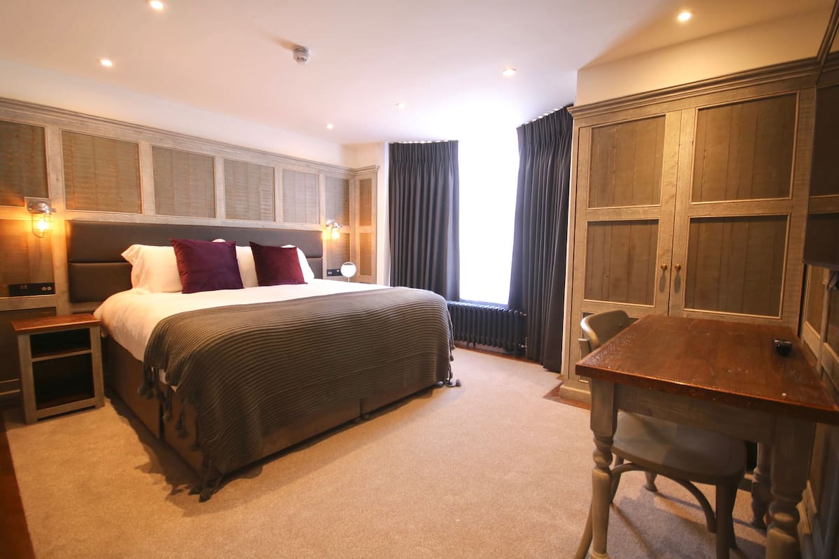 A bedroom with a large bed, bedside tables, a wooden wardrobe, and a small table with a chair.