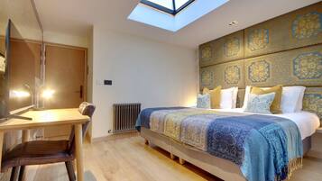 A bedroom with a skylight, a bed with patterned bedding, a bedside table, and a chair.