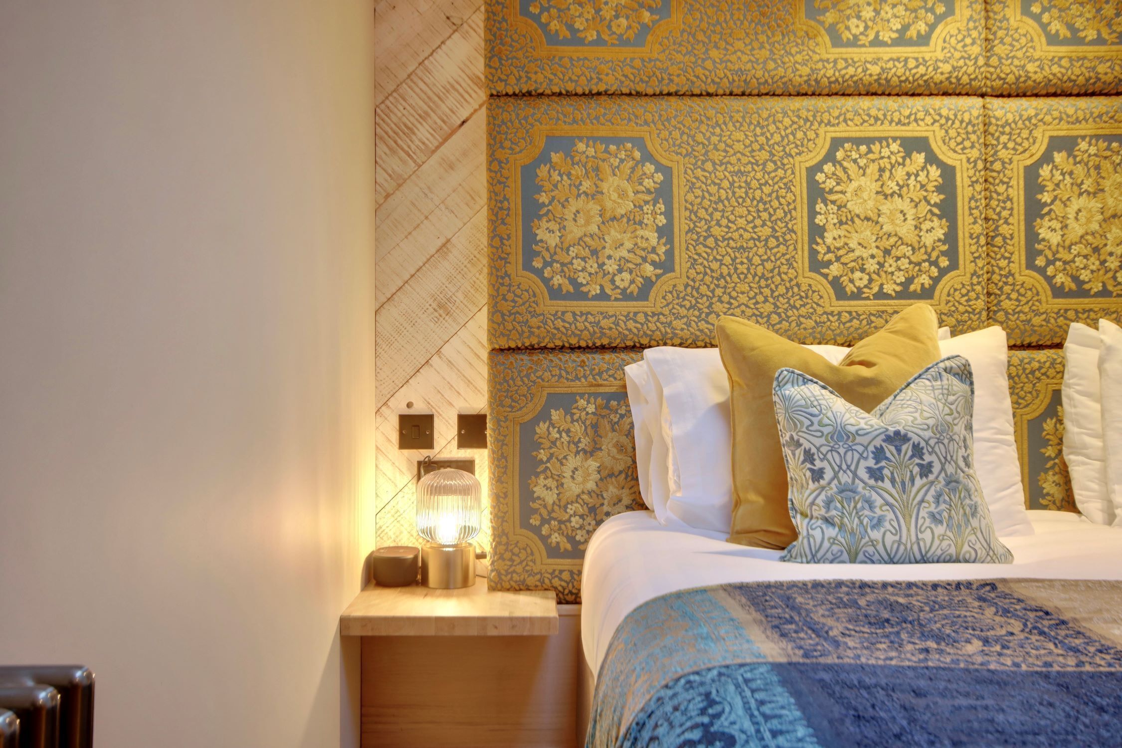 A neatly made bed with patterned bedding, a bedside table with a lamp, and a decorative headboard.