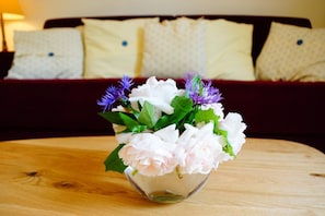 A clear glass vase with white and pink flowers and purple blooms on a wooden table.