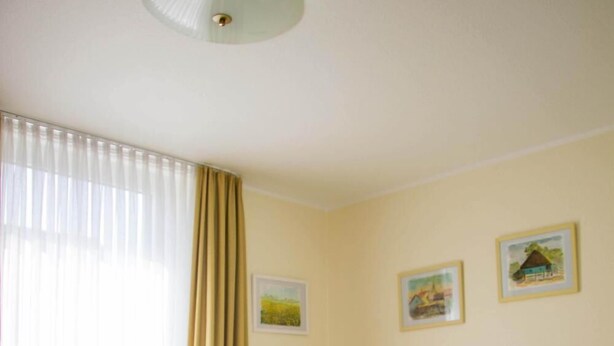 Hotellihuone, jossa on suuri sänky, kattovalaisin ja kaksi kehystettyä kuvaa seinällä.