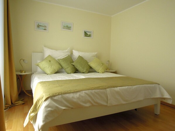 A neatly made bed with a white and green color scheme, a small bedside table with a lamp, and two framed pictures on the wall.