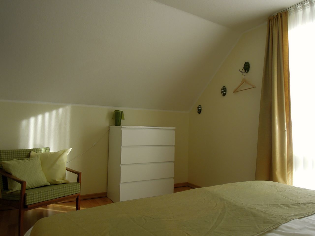 Une chambre à coucher avec un lit, une commode, une chaise et une fenêtre avec des rideaux.