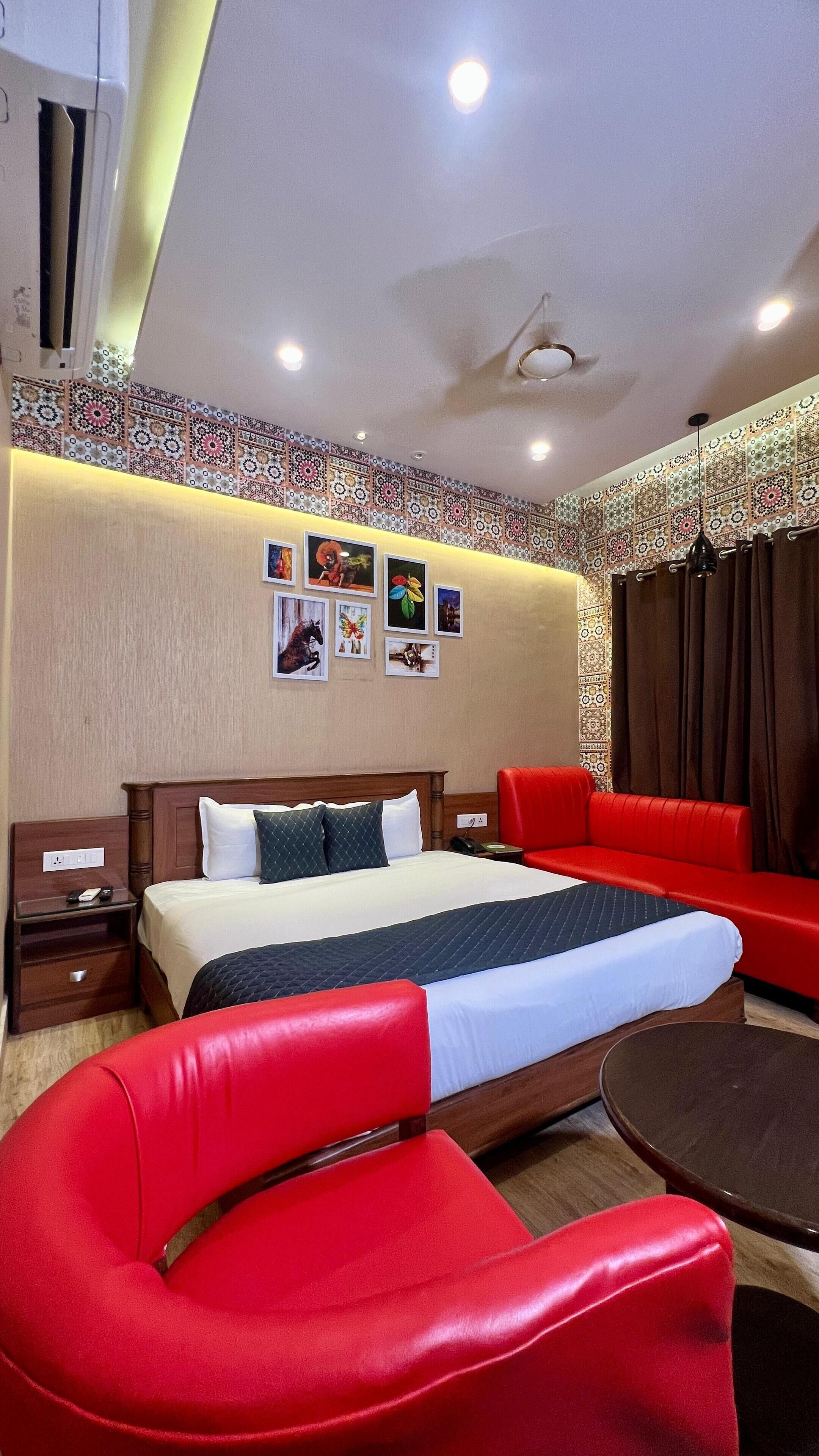 A hotel room with a large bed, red chairs, a small table, and a wall decorated with framed pictures.