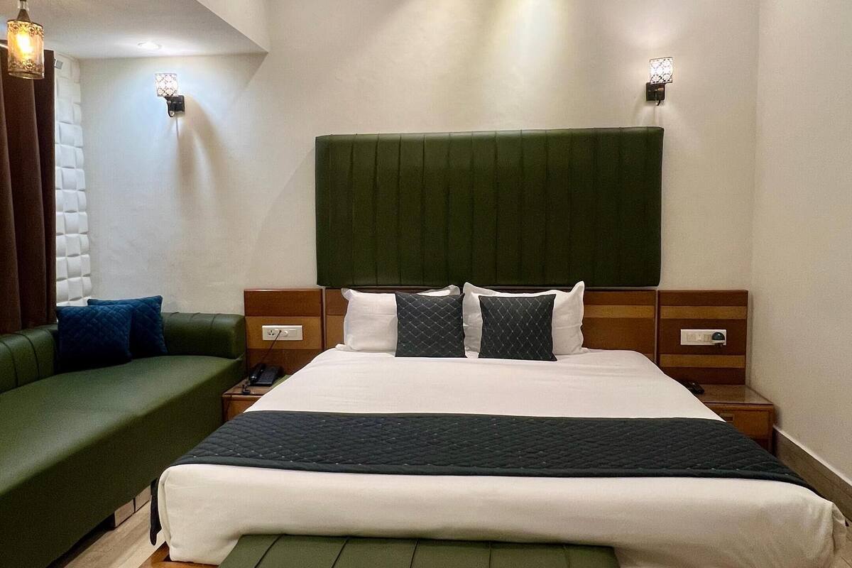 A modern hotel room with a large bed, green upholstered furniture, and recessed ceiling lighting.