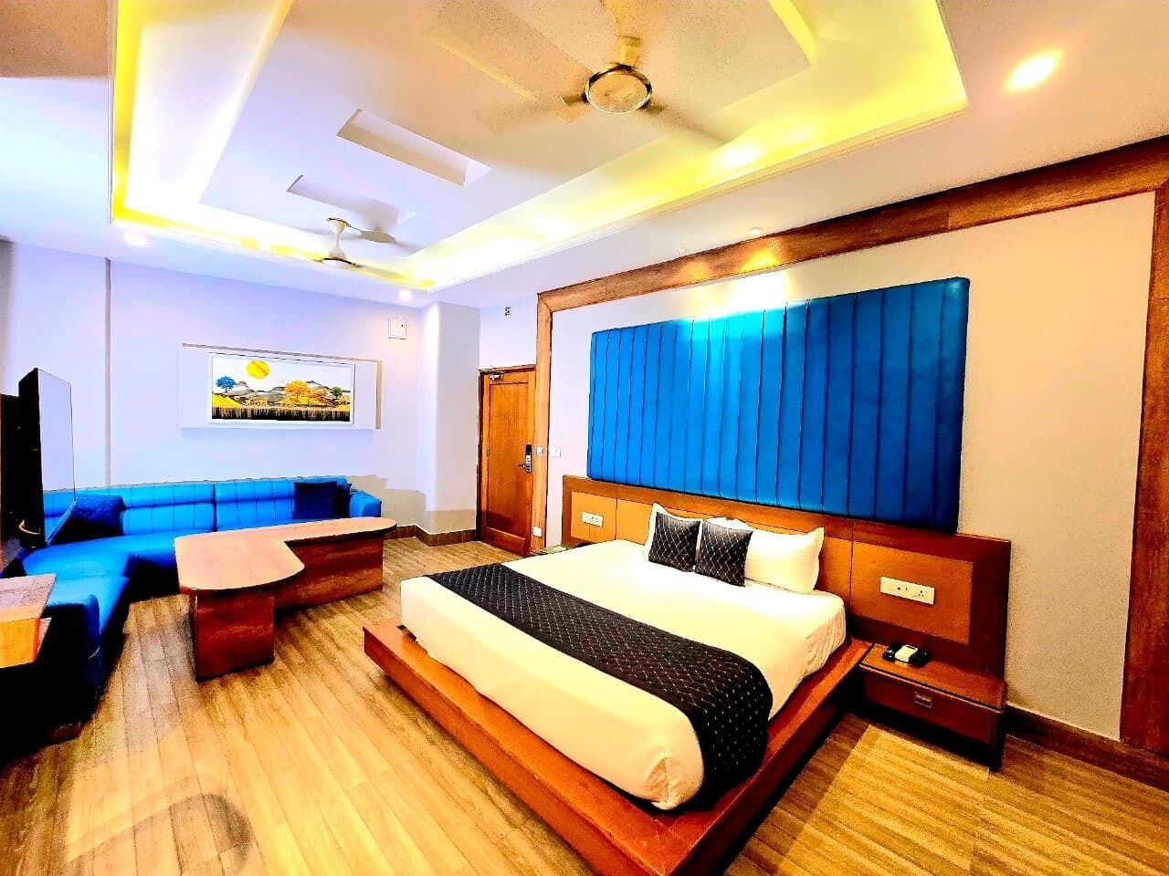 A hotel room with a large bed, a sofa, a small table, and a ceiling fan.