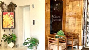 Un área de recepción con un panel de madera, un retrato enmarcado y dos sillas de madera con una planta en maceta.