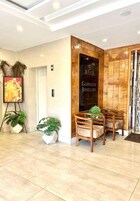 Un área de recepción con un panel de madera, un retrato enmarcado y dos sillas de madera con una planta en maceta.