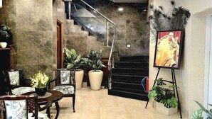 Un vestíbulo amplio con piso de mármol, una escalera y una zona de estar con sillas y una mesa.