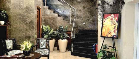 Un vestíbulo amplio con piso de mármol, una escalera y una zona de estar con sillas y una mesa.