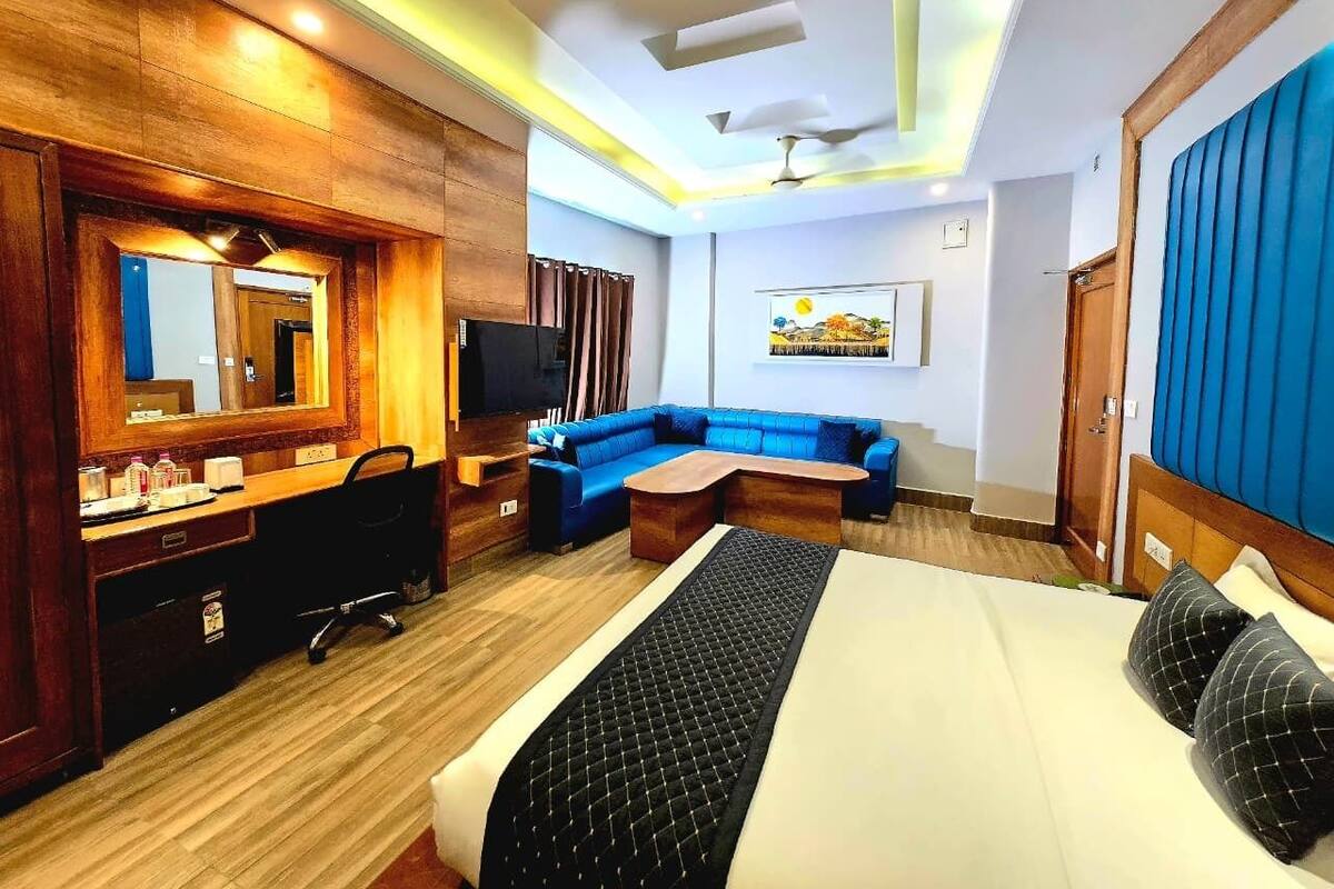 A hotel room with a bed, a sofa, a desk with a mirror, and a television.
