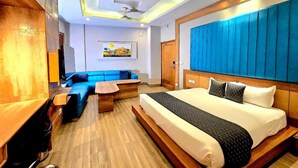Una habitación de hotel moderna con una cama grande, un sofá tapizado en azul, una mesa de centro de madera y un ventilador de techo.