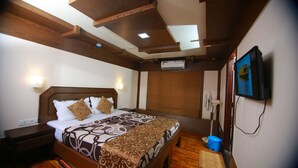 A hotel room with a wooden bed, a nightstand, a wall-mounted air conditioner, a ceiling fan, and a television. - My Trip Houseboat (Kuttanad Taluk)