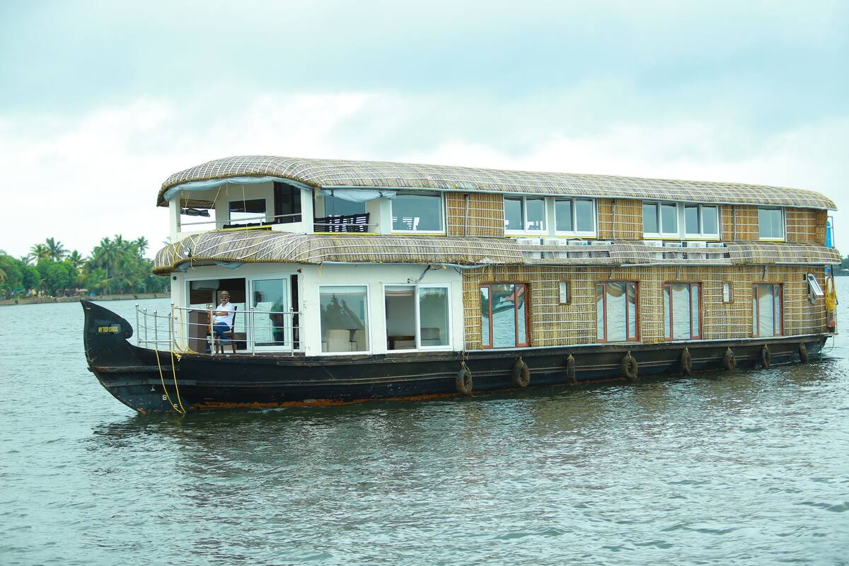 A houseboat with a two-story structure, large windows, and a covered deck area.