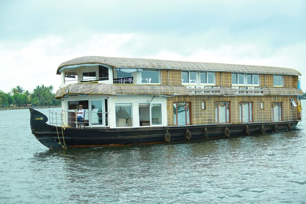Una casa flotante con estructura de dos pisos, ventanas grandes y terraza cubierta.