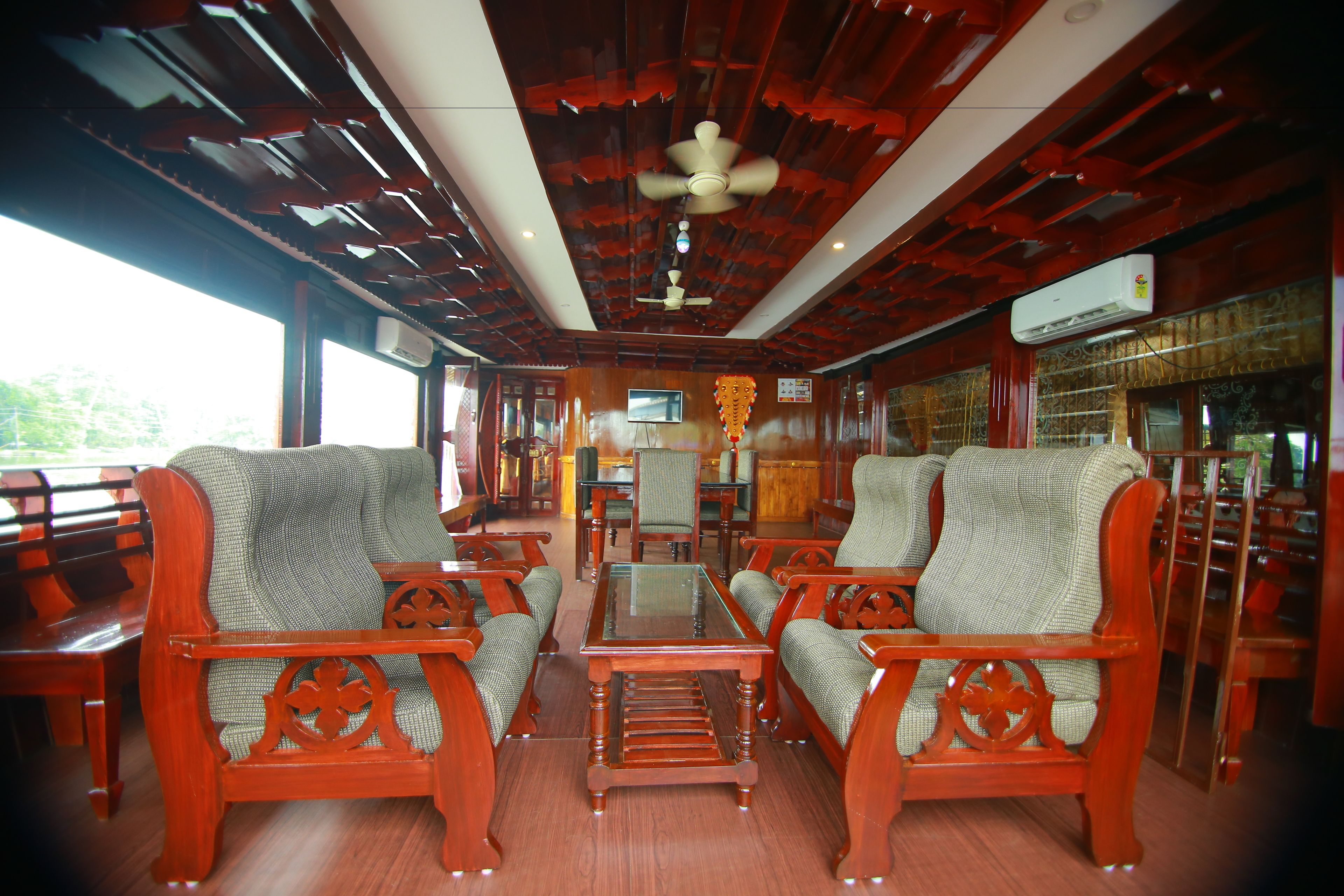 A wooden-furnished interior with a ceiling fan, a glass table, and upholstered chairs.