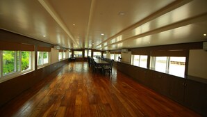 A spacious room with wooden flooring, large windows, and a long table with chairs. - My Trip Houseboat (Kuttanad Taluk)