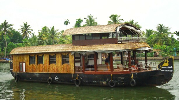 A houseboat with a wooden exterior, a covered upper deck, and a small balcony. - My Trip Houseboat (Kuttanad Taluk)
