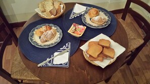 A round wooden table with four plates of food, including pastries and bread, arranged on a blue placemat. - Miseria e Nobiltà (Naples)
