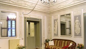 A room with a wooden floor, a striped sofa, a table with a vase, and a chandelier. - Miseria e Nobiltà (Naples)