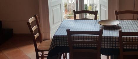 Zona pranzo con tavolo apparecchiato per quattro persone, sedie, vista su un balcone esterno tramite una porta in vetro e un lampadario a parete.