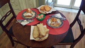 A dining table with plates of pastries, bread, and a small bowl of fruit. - Miseria e Nobiltà (Naples)
