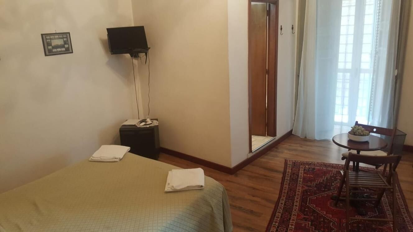 Ein Hotelzimmer mit einem Bett, einem Nachttisch, einem Spiegel, einem Fernseher und einem Fenster mit Vorhängen.