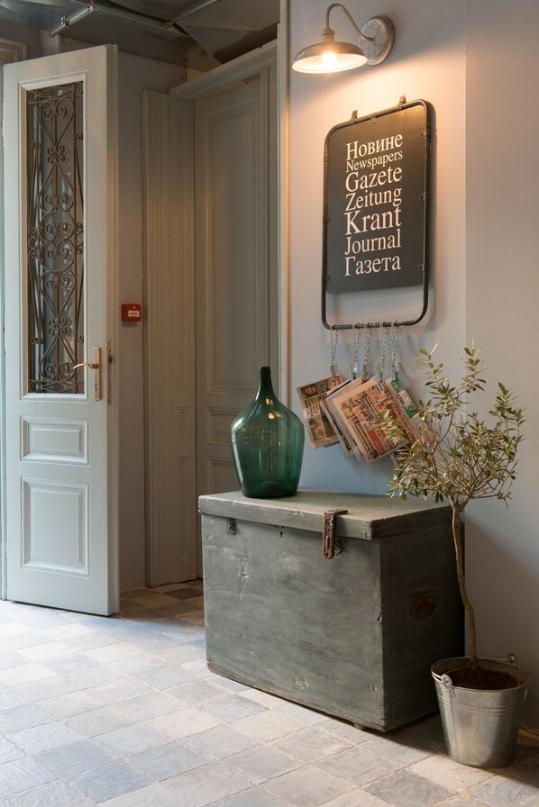 A hallway with a vintage suitcase, a green vase, and a wall-mounted sign with foreign text.