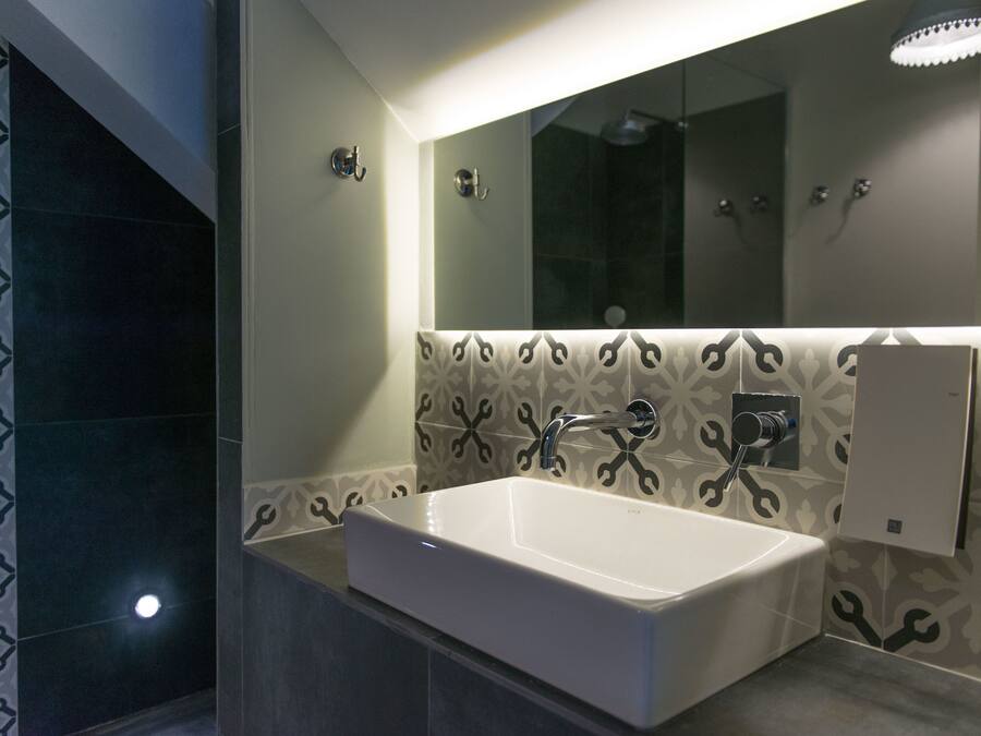 Un baño moderno con un lavamanos rectangular, un espejo grande y un revestimiento de pared con diseño.