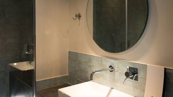 A modern bathroom with a rectangular sink, a round mirror, and a shower area.
