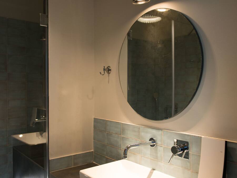 A modern bathroom with a rectangular sink, a round mirror, and a shower area.
