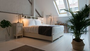 Een moderne slaapkamer met een bed, nachtkastjes, een bureau en een grote potplant.