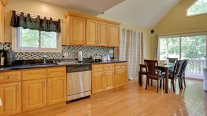 A kitchen with wooden cabinets, a dishwasher, and a dining area with a table and chairs. - Pools, Hot Tub & More: Bushkill Mountain Getaway! (Bushkill)