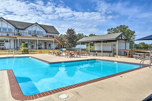 A swimming pool with a brick border, outdoor seating, and a covered area with a roof.