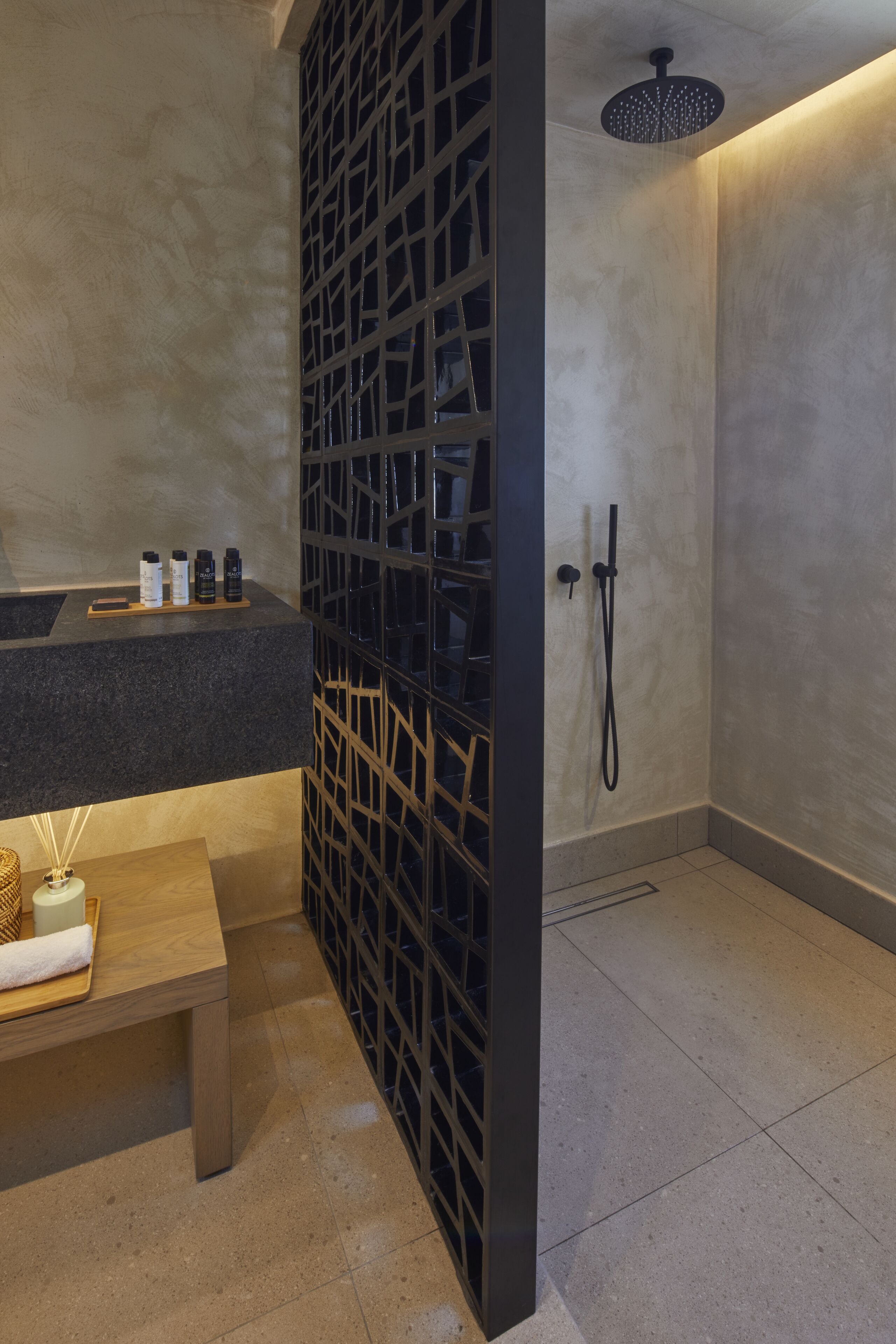 A modern bathroom with a shower, a sink with toiletries, and a wooden bench.