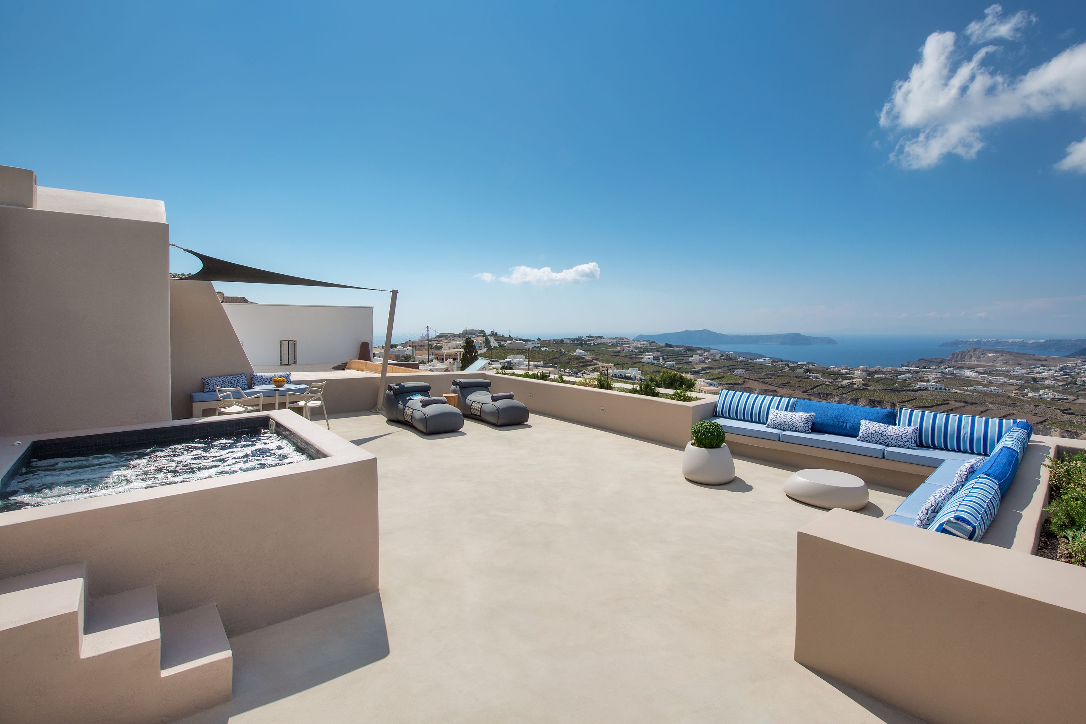 A rooftop terrace with a hot tub, seating area, and a view of the city and sea.