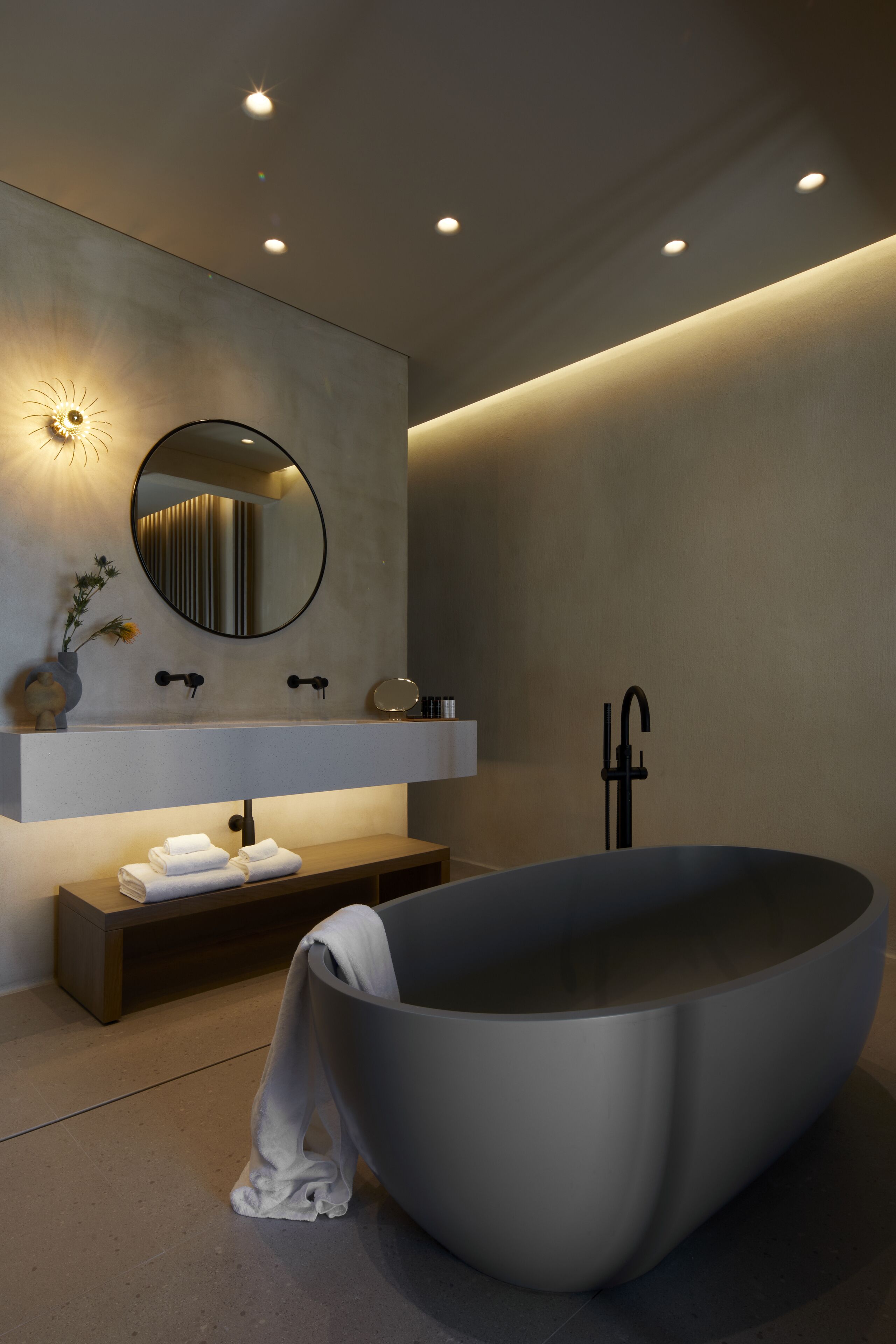 A modern bathroom with a freestanding bathtub, a round mirror, and a minimalist vanity.