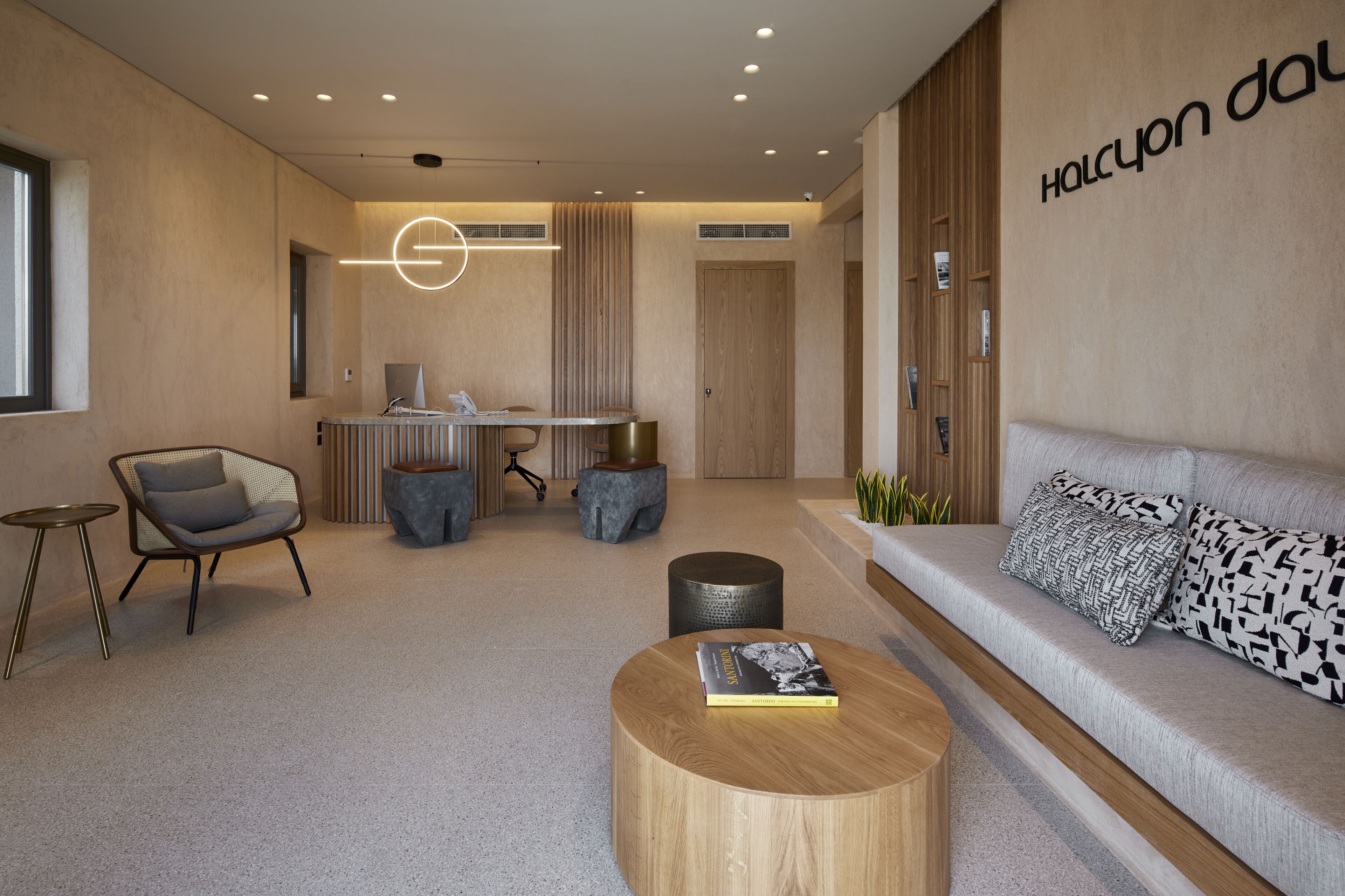 A modern reception area with a sofa, a round wooden table, a chair, and a desk with a computer.
