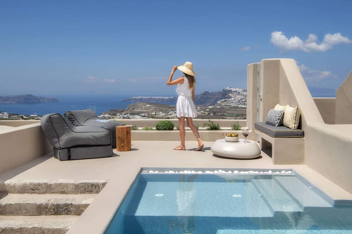 A pool area with a view of the sea, a lounge chair, and a small seating area with cushions.