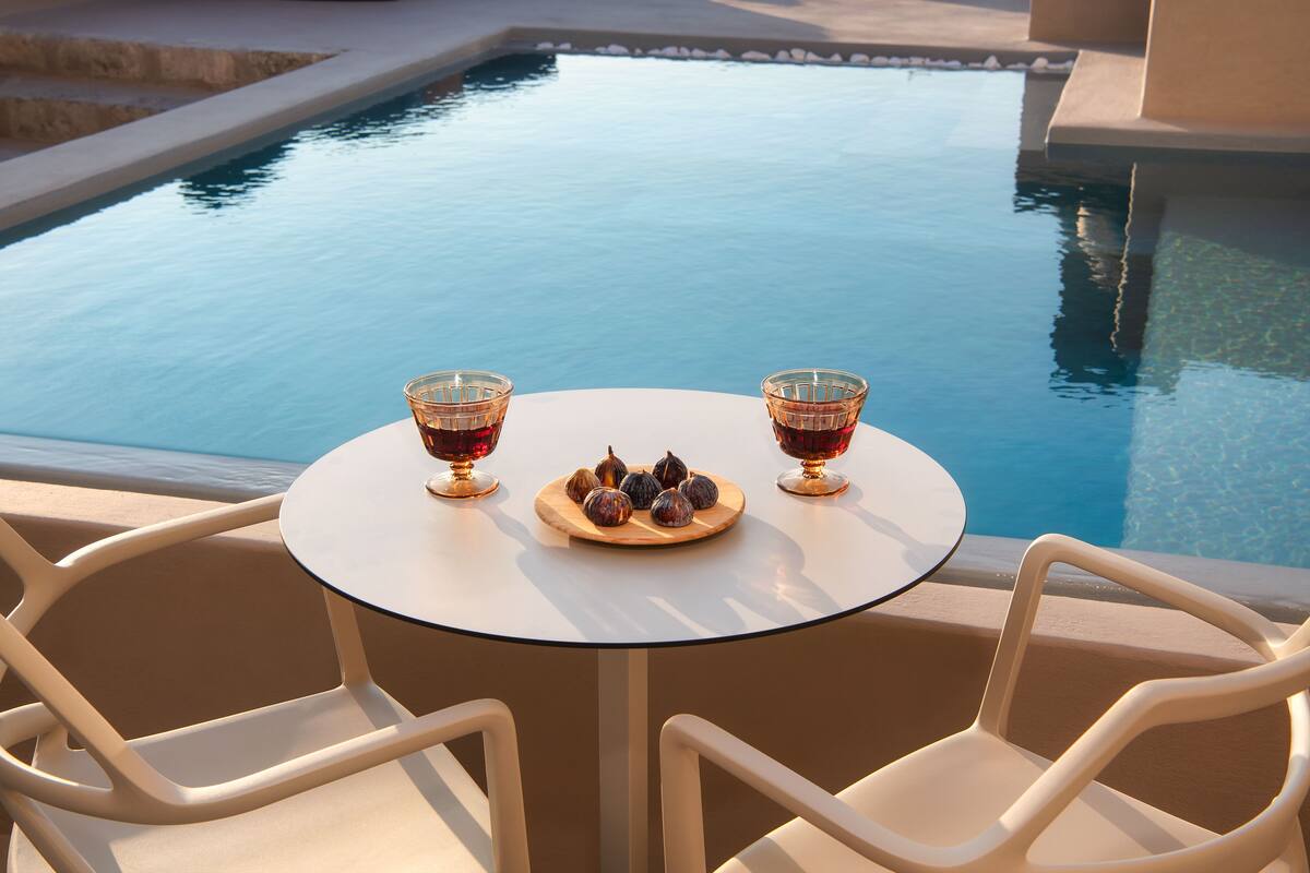 A round table with two chairs and a plate of figs, positioned by a pool.