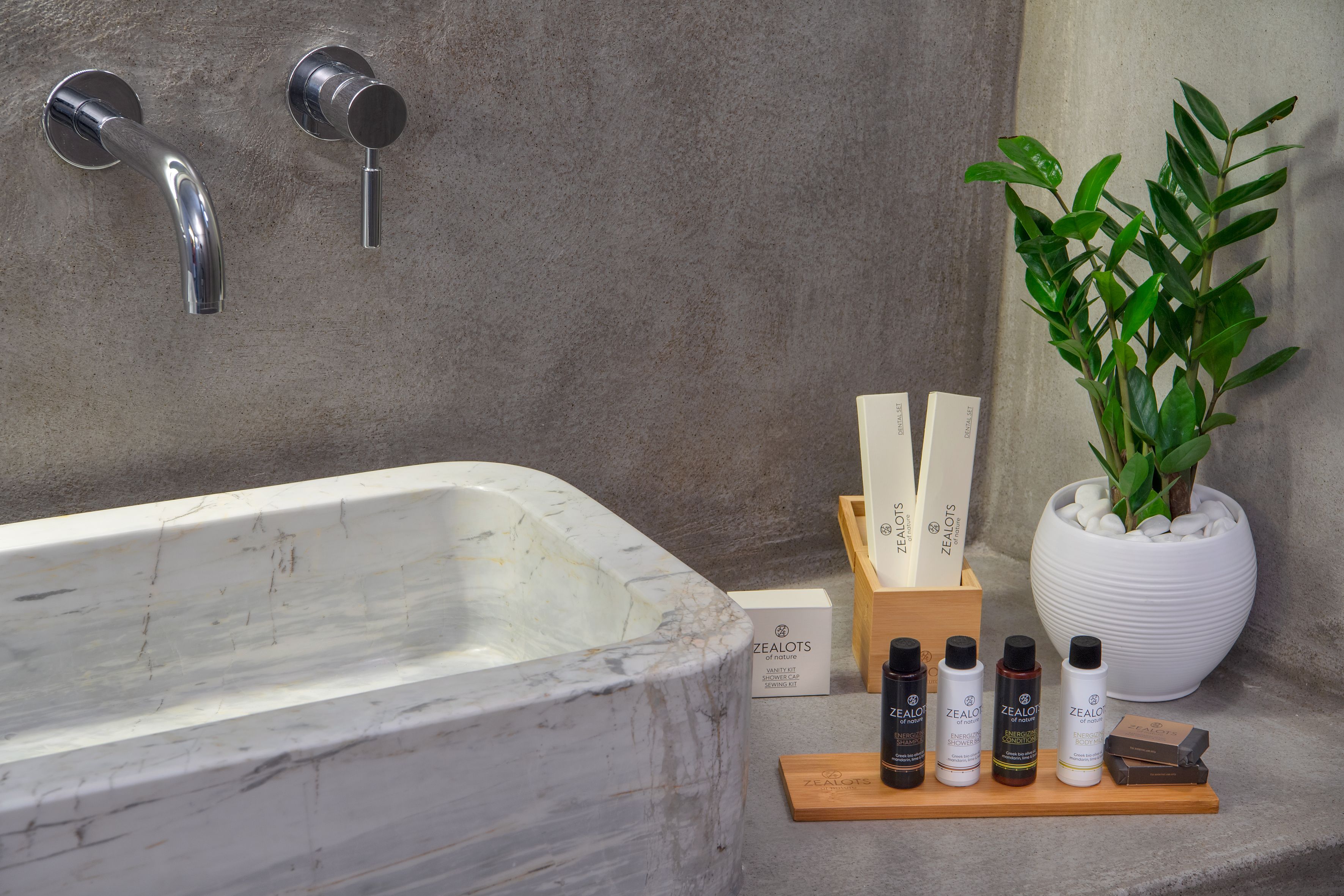 Une salle de bain avec une baignoire en marbre, une plante en pot et une étagère en bois où sont rangés des produits de soins pour la peau.