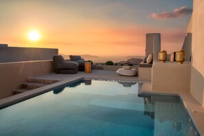 A rooftop infinity pool with a sunset view, lounge chairs, and decorative vases. - Halcyon Days Suites (Santorini)