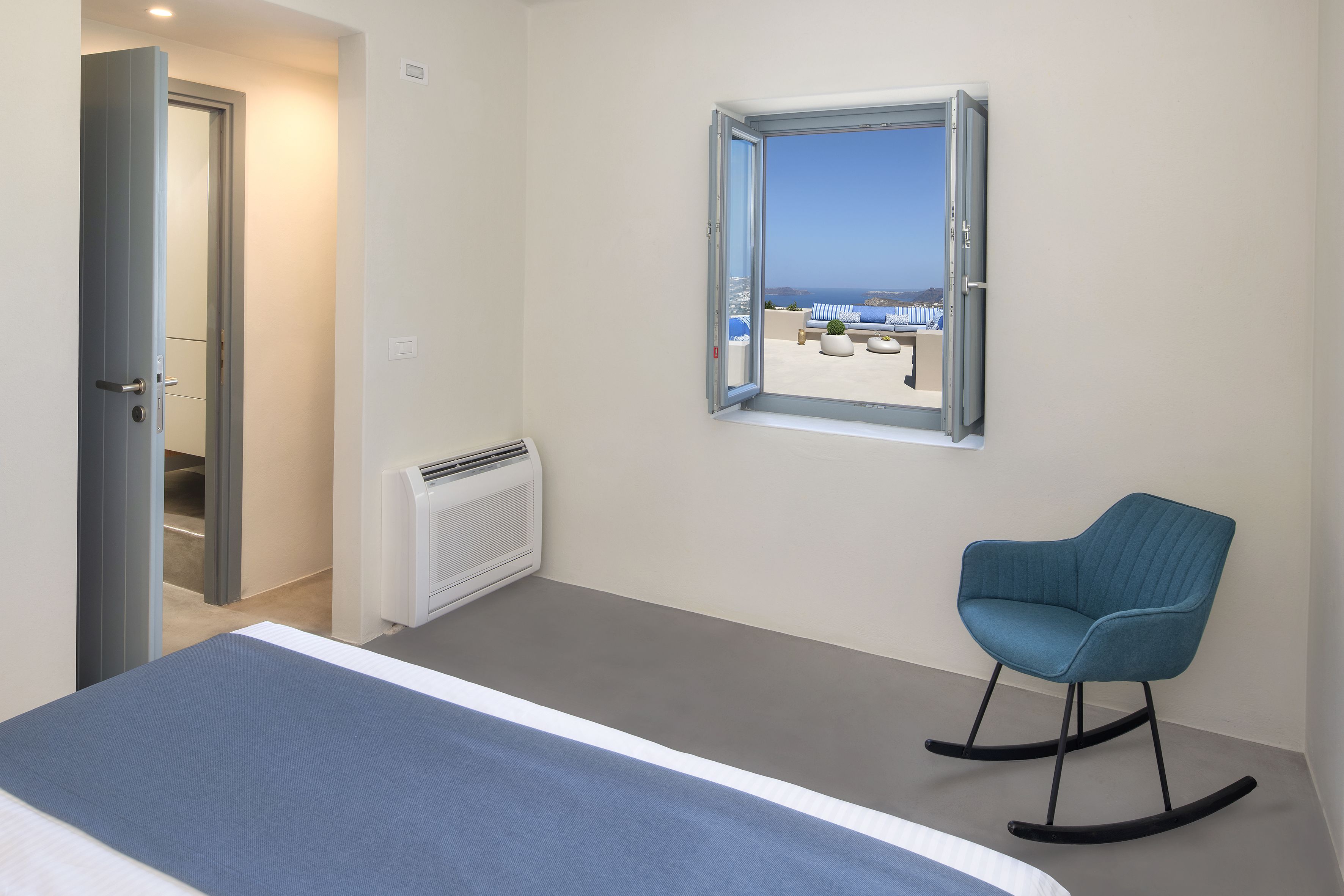 A bedroom with a bed, a rocking chair, a window with a view of the beach, and a door leading to another room.