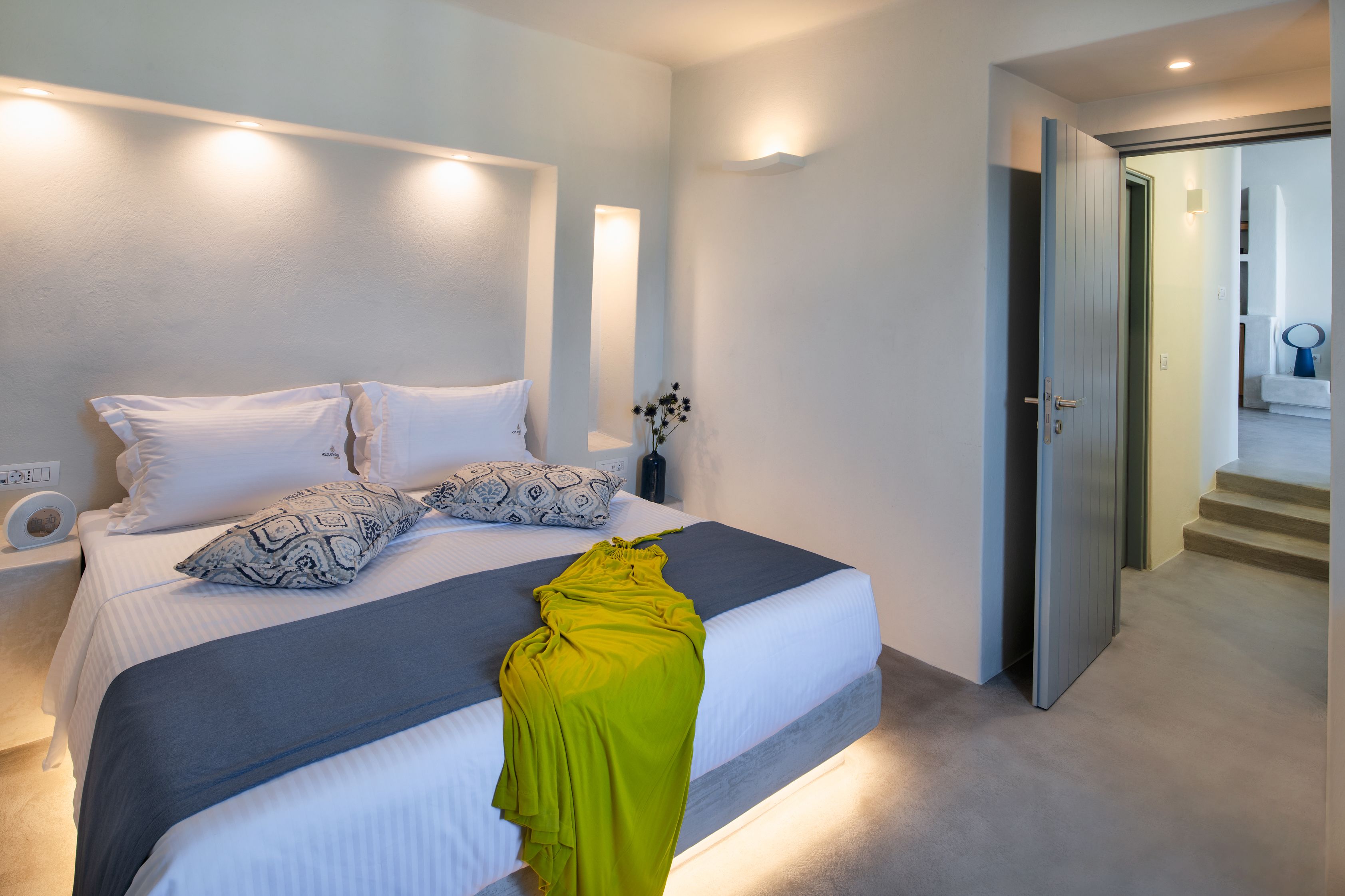 A modern bedroom with a large bed, bedside lamps, and a view of a staircase.