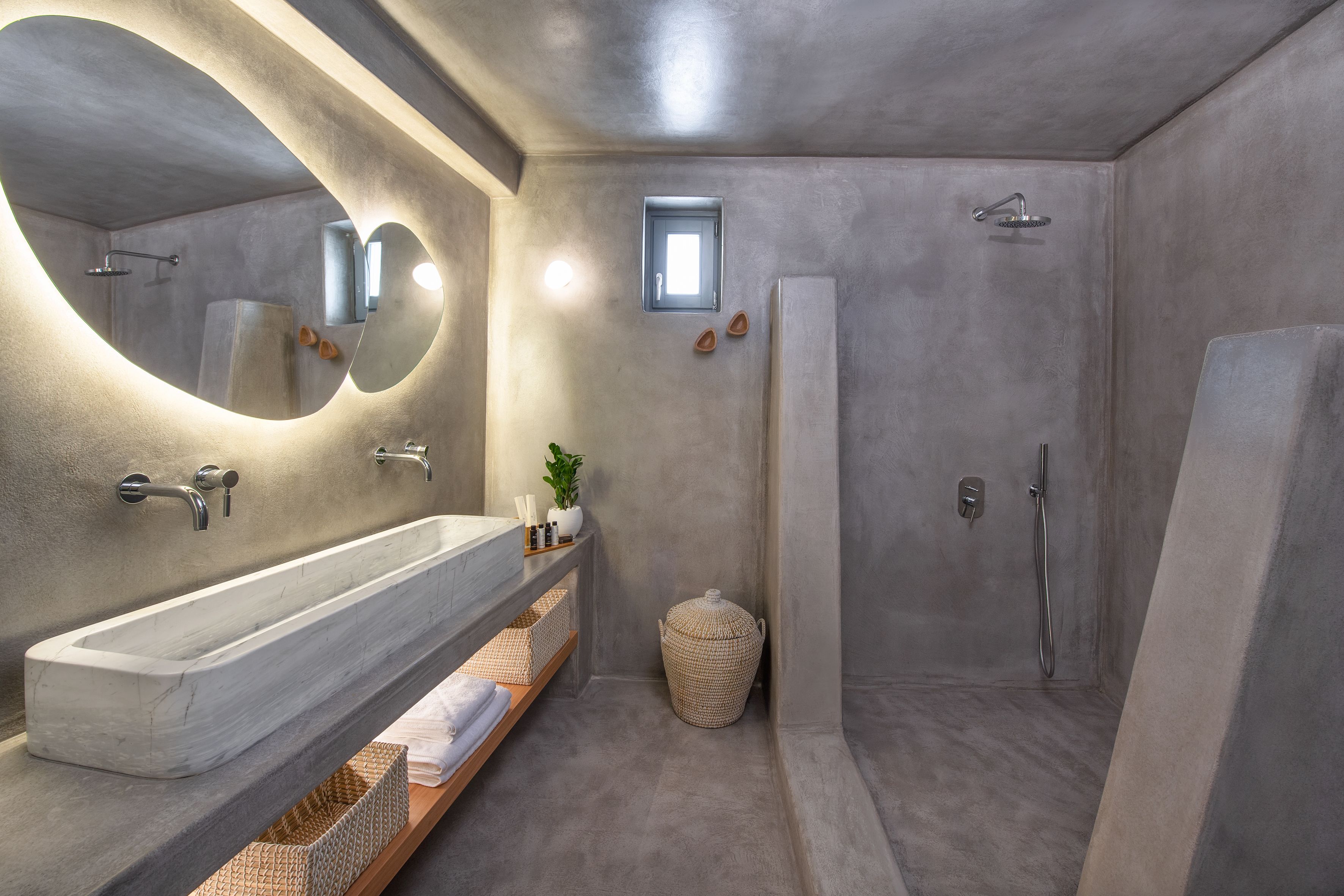 Une salle de bain moderne avec un grand lavabo en marbre, une douche à l’italienne et une petite fenêtre.