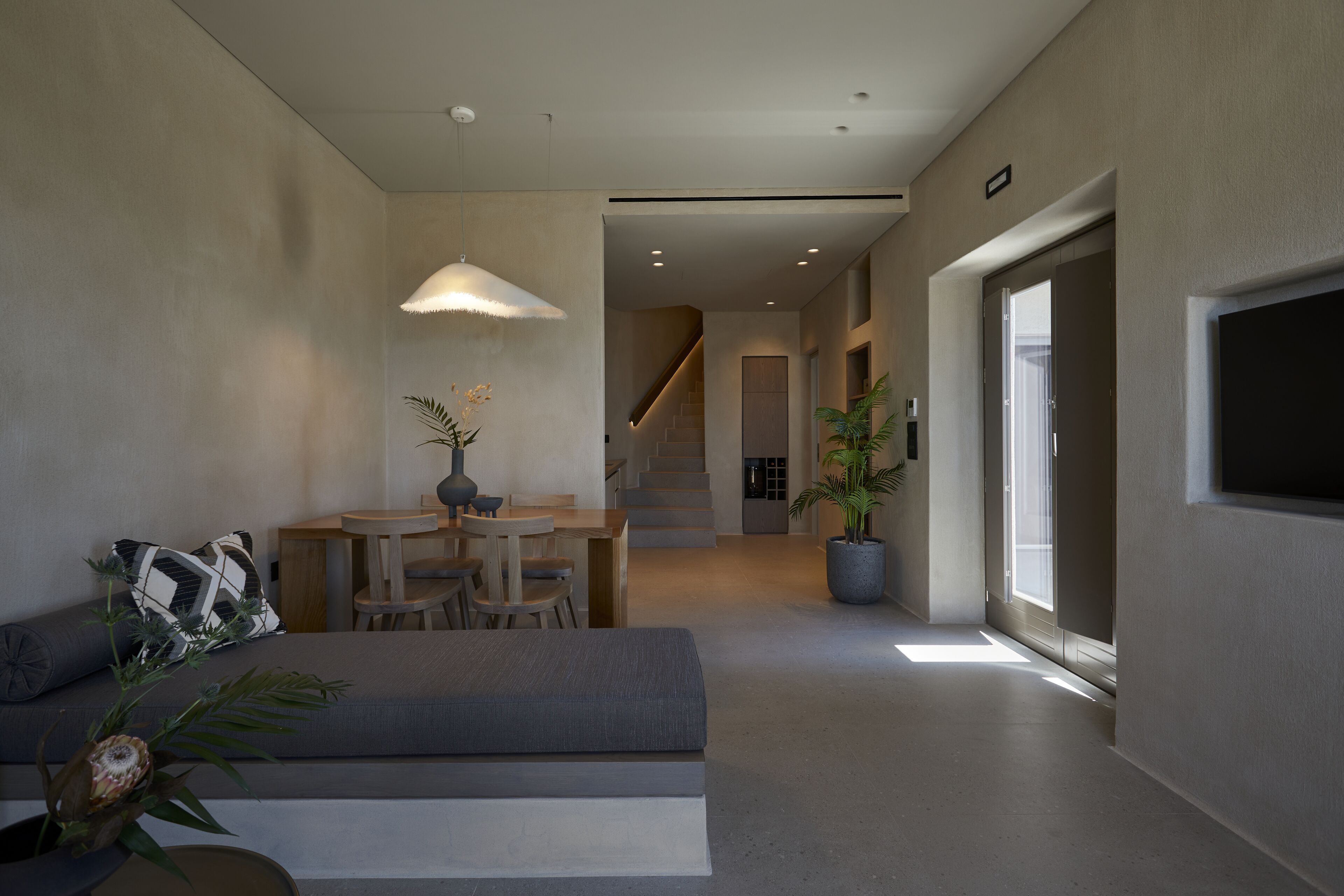 A modern living room with a sofa, dining table, and chairs. There is a staircase leading to another level.