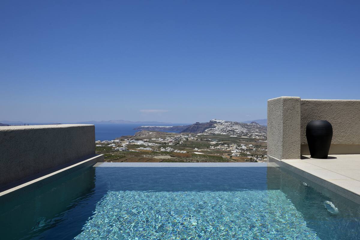 An infinity pool with a clear view of a coastal town and mountains in the background.