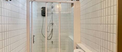A bathroom with white tiled walls, a glass-enclosed shower, a toilet, and a wooden vanity.