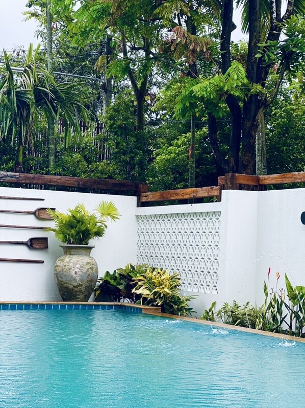 A pool surrounded by lush greenery and a white wall with a lattice design. - Tai resort (San Pa Thong)